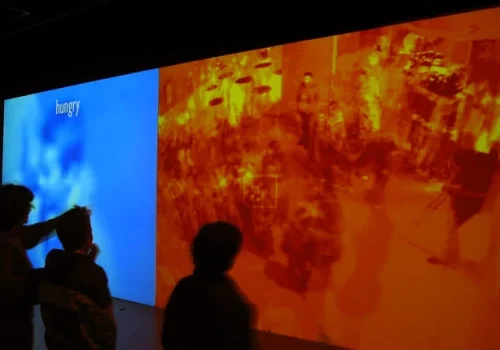 Photo de l'œuvre Taken, par David Rokeby. Installation interactive, réalisée en 2002. Trois silhouettes de visiteurs devant un mur de projection vidéo. Présentée lors de l'Évènement culturel SYNTHETIC TIMES - Media Art China, en 2008.